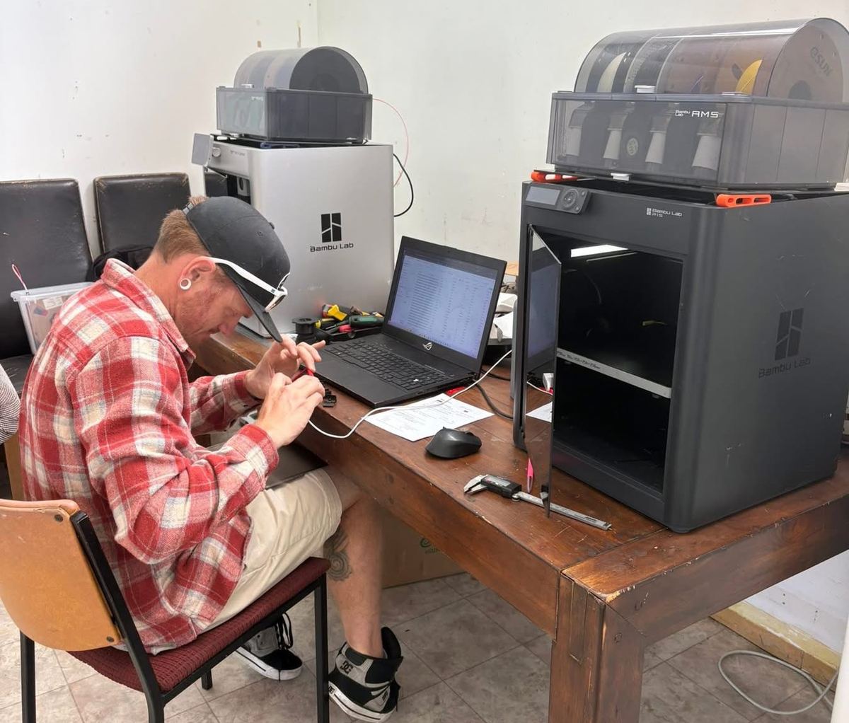 Joe at Taupō's Repair Cafe, mending gear with two Bambu Lab printers on hand